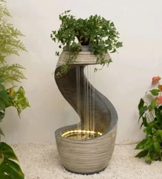 a water fountain with a plant in it and lights on the bottom, surrounded by potted plants