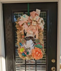 a wreath with flowers and ribbons hanging on the front door to welcome someone in need