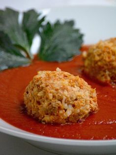 two balls of food on a plate with tomato sauce and parsley leaves in the background