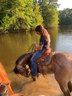 a woman riding on the back of a brown horse across a river covered in mud