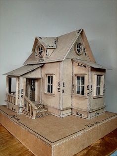 a cardboard model of a house on top of a wooden table with measurements in front of it