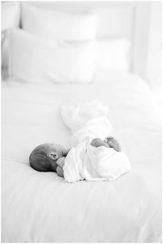 a baby wrapped in a blanket laying on top of a white bed covered in blankets