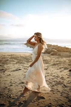 a woman standing on top of a sandy beach next to the ocean wearing a white dress