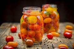 several jars filled with tomatoes on top of a wooden table next to small red and yellow tomatoes