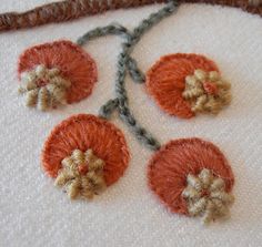 four orange flowers on a white cloth with black thread in the middle and brown trim around them