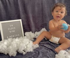 a baby in diapers holding a blue ball and sitting on a bed with cotton