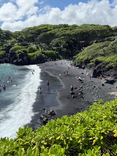 many people are swimming in the water at this black sand beach with lush green vegetation