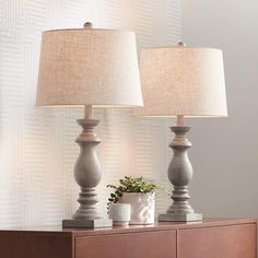 two lamps sitting on top of a dresser next to a potted plant and lamp shade