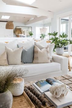 a living room filled with white furniture and lots of plants on top of a wooden table