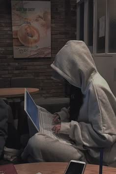 two people sitting at a table with laptops in front of them, one person wearing a hoodie