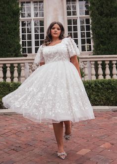 a woman in a white dress is standing on a brick walkway and posing for the camera