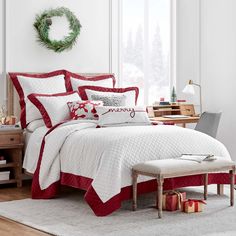 a bed with red and white comforters in a room next to a window, christmas wreath on the wall