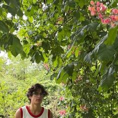 a young man standing in front of a tree with pink flowers on it's branches