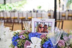 a table topped with blue and purple flowers next to wineglasses on top of a white table cloth