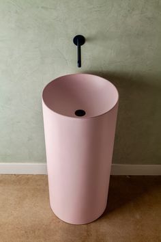 a pink trash can sitting in front of a wall with a black hook on it