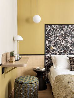 a bedroom with yellow walls and a floral wallpaper on the headboard, along with a small round foot stool