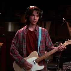 a young man playing an electric guitar in a recording studio, with headphones on