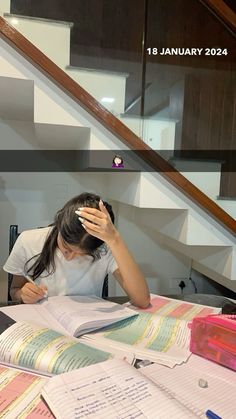 a woman sitting at a table with books and papers in front of her, reading