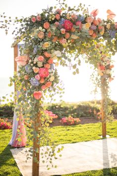 an outdoor ceremony with flowers and greenery on the arch, in front of the ocean