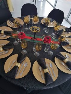 the table is set with gold and black plates, silverware, and rose centerpieces