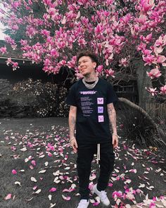 a man standing in front of a tree with lots of pink flowers on the ground