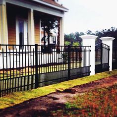 a black iron fence in front of a house with two white pillars on each side