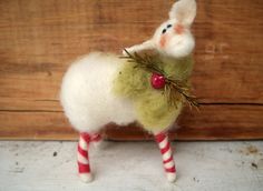 a white sheep with a red and green decoration on it's back standing in front of a wooden wall