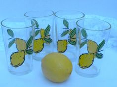 four glasses with lemons and leaves painted on the glass are next to an orange