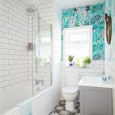 a white toilet sitting next to a bath tub under a bathroom window filled with potted plants