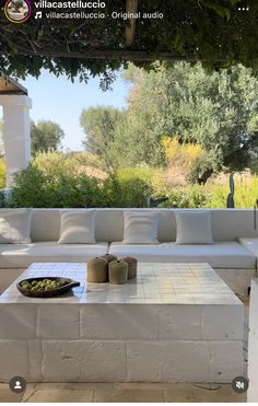 a white couch sitting under a tree next to a table on top of a stone floor