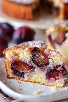 a close up of a piece of cake on a plate with plums in the background