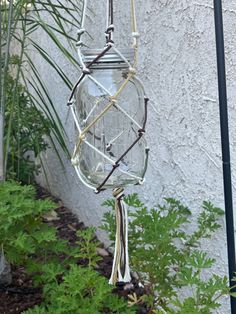 a glass jar hanging from the side of a building next to some plants and flowers