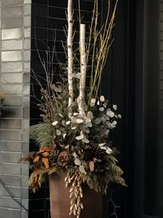 a tall planter filled with lots of branches and flowers next to a brick wall