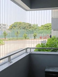 an empty balcony with plants and trees in the back ground, looking out onto a parking lot