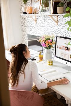 a woman sitting in front of a computer on top of a white desk with flowers