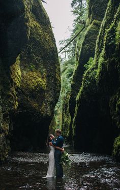 a bride and groom standing in the middle of a river surrounded by mossy rocks