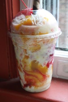 an ice cream sundae in a plastic cup on a window sill with a straw