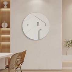 a white clock mounted to the side of a wall next to a table and chair