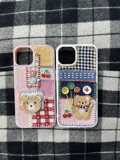 two cell phones sitting next to each other on a plaid cloth covered surface with teddy bears and cherries