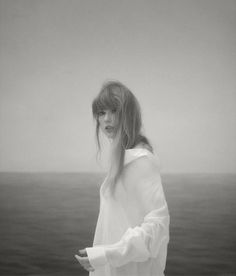 a black and white photo of a woman with long hair standing in front of the ocean