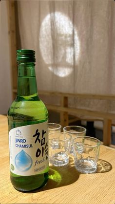 a bottle of water sitting on top of a wooden table next to shot glasses and a curtain