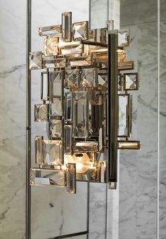 a modern chandelier with crystal cubes hanging from it's sides in front of a marble wall