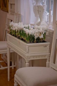 a white table with flowers on it in front of a chair and another piece of furniture