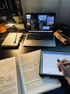 a person is writing on a notebook and using a tablet with a laptop in front of them