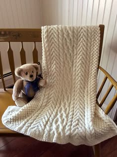 a teddy bear sitting on top of a wooden chair under a white knitted blanket