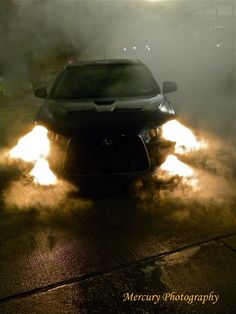 a car with flames coming out of it's hood driving down the street at night