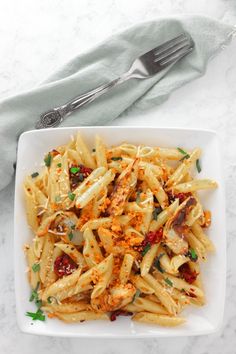 a white plate topped with pasta covered in sauce next to a fork and napkin on top of a marble table