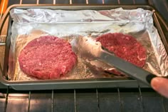 two hamburger patties being cooked in an oven with a spatula and tongs