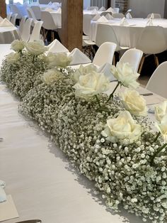 white flowers and baby's breath are arranged in the center of a long table