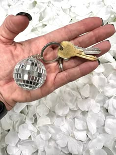 a person's hand holding two keys and a disco ball keychain in front of white flowers